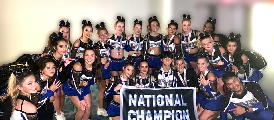 Legit 4 earned first place finish and championship rings! Cheer team smiling holding a award banner.
